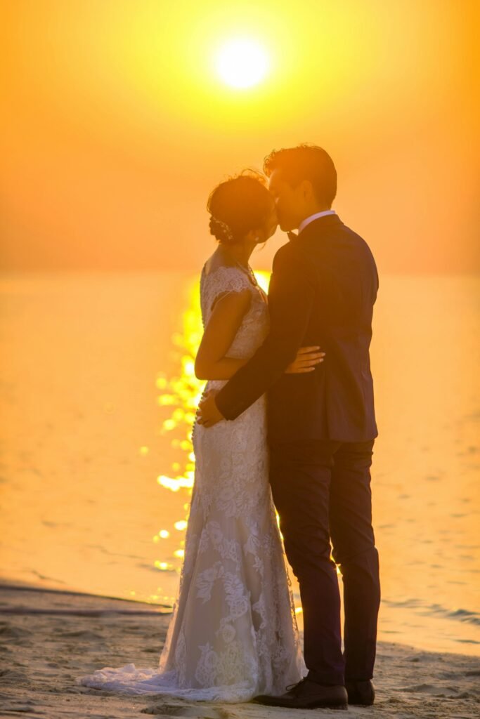 Captivating moment of a couple sharing a kiss during a beach sunset wedding, exuding romance.